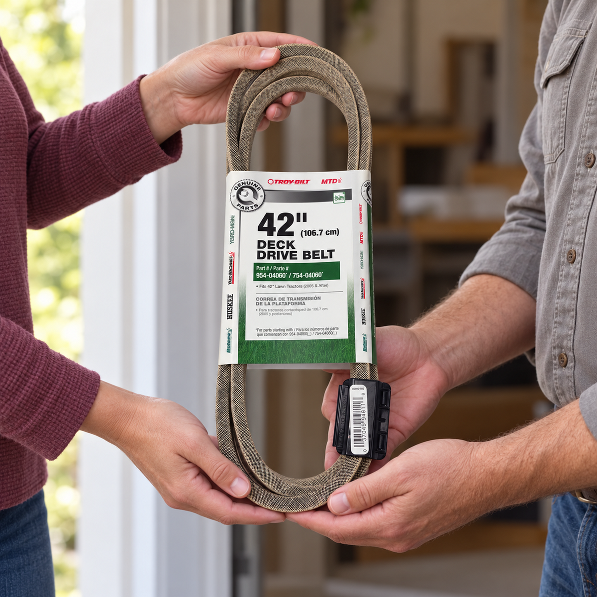 Two adults pass the packaged Troy-Bilt and MTD deck belt between them at a workshop doorway.