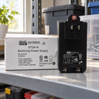 AI-generated lifestyle illustration of the unplugged MG ST241A power supply and original box in a dry utility-shelf setting.