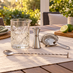 AI-generated lifestyle illustration of the four-piece Silver One cocktail mixing set on a linen-covered patio table.