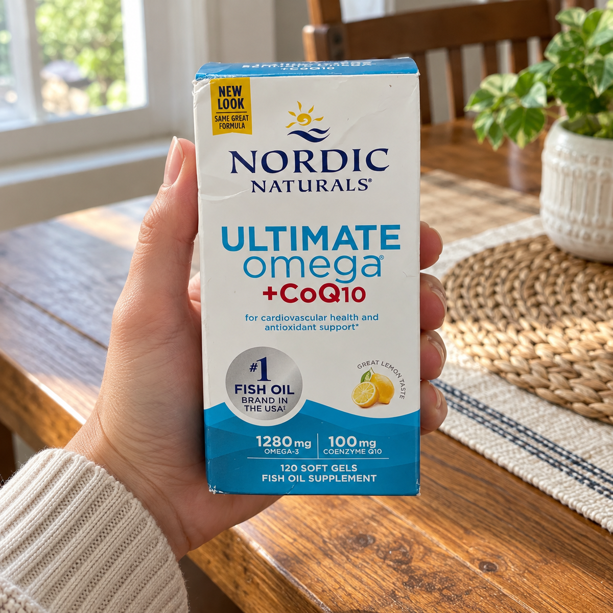 An adult holding the Nordic Naturals Ultimate Omega + CoQ10 120-soft-gel box at a dining table