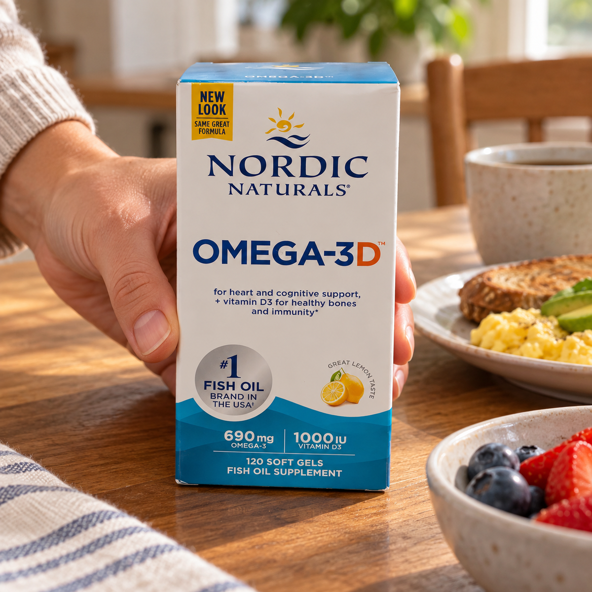 An adult setting a Nordic Naturals Omega-3D 120-soft-gel box beside breakfast