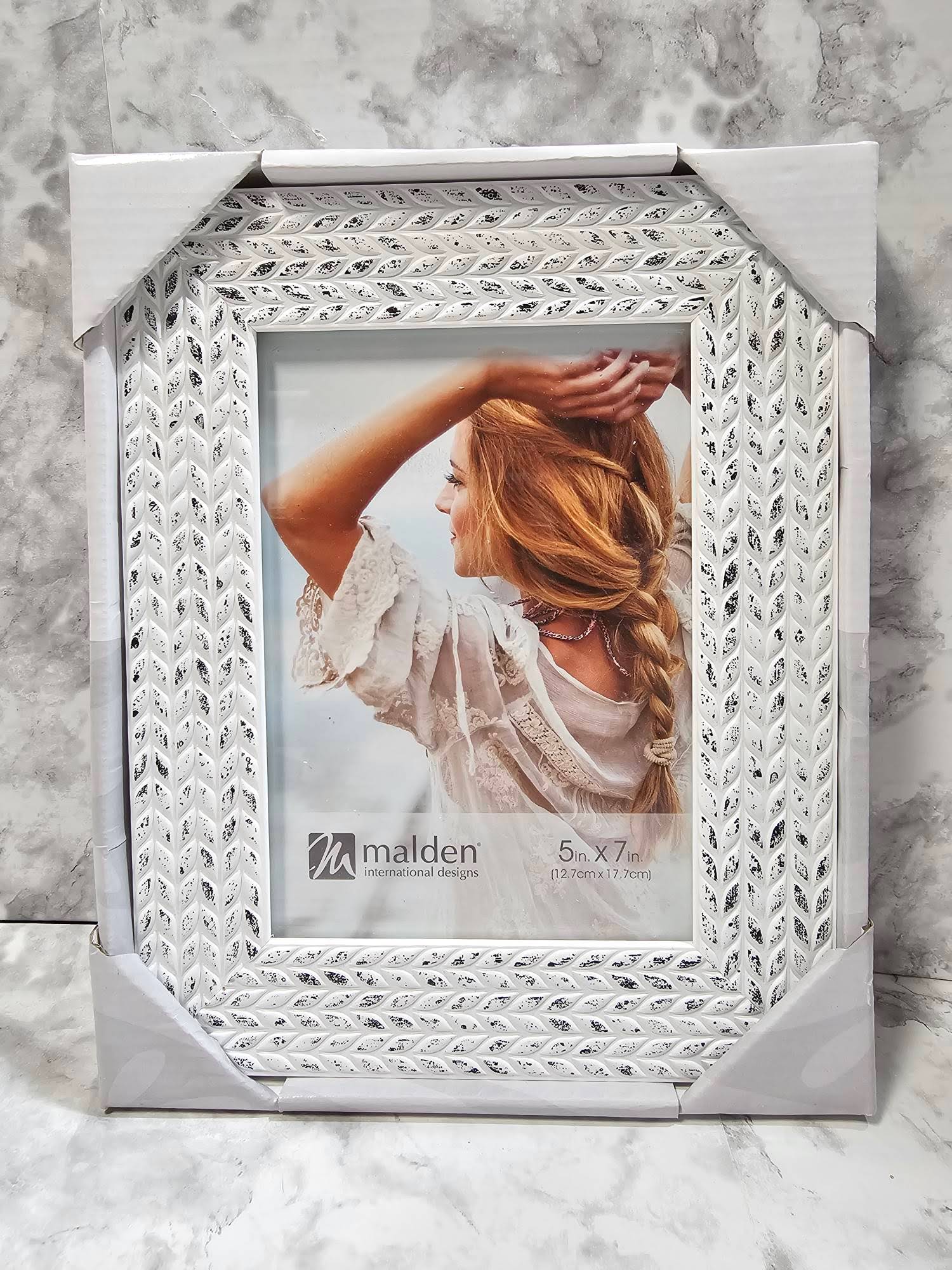 Decorative white photo frame with intricate patterns on a marble surface