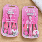 Two pink Gillette Venus Sensitive three-count razor packs on pale wood beside a white towel