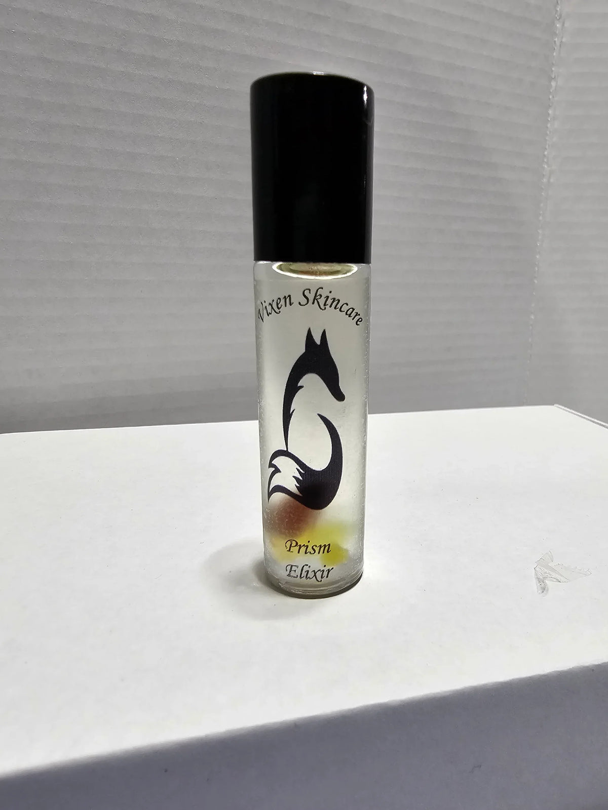 Vixen Prism Elixir roller bottle with a black cap and visible crystals on a white surface.