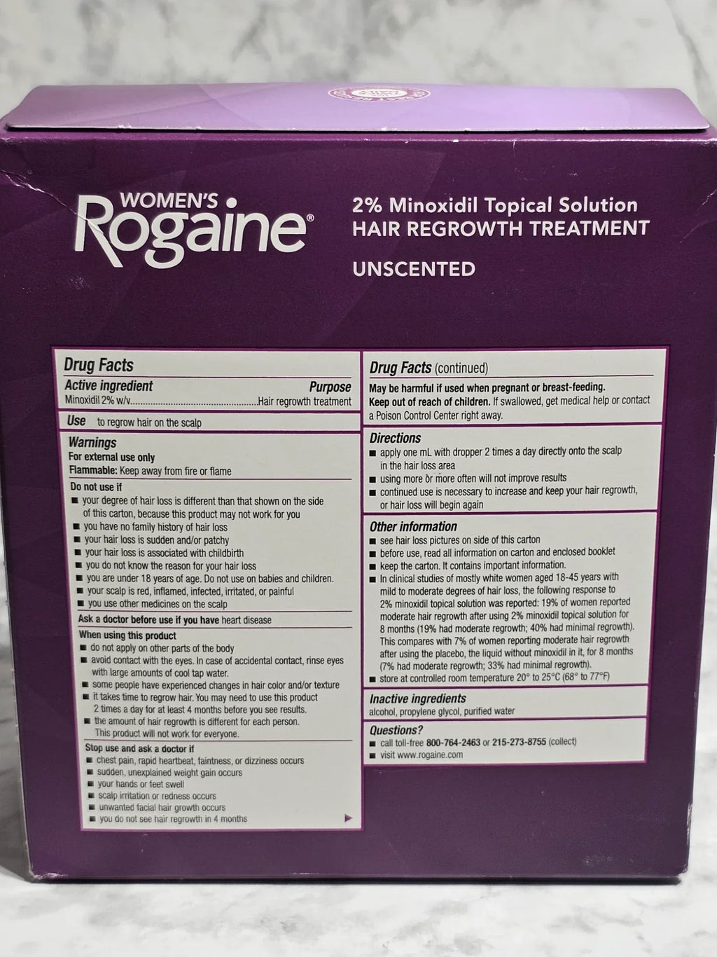 Purple box of Women's Rogaine hair regrowth treatment on a marble surface