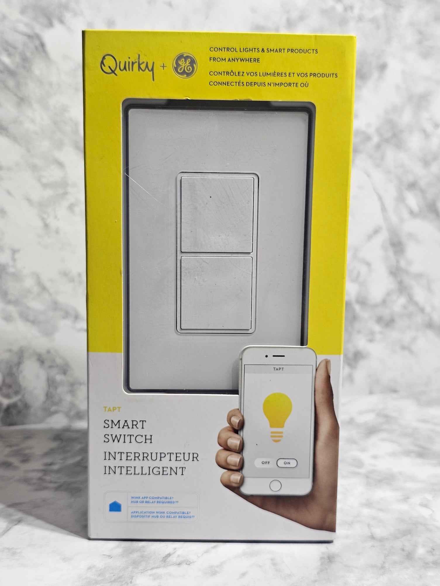 Quirky smart switch packaging with a hand holding a smartphone displaying a light bulb icon.
