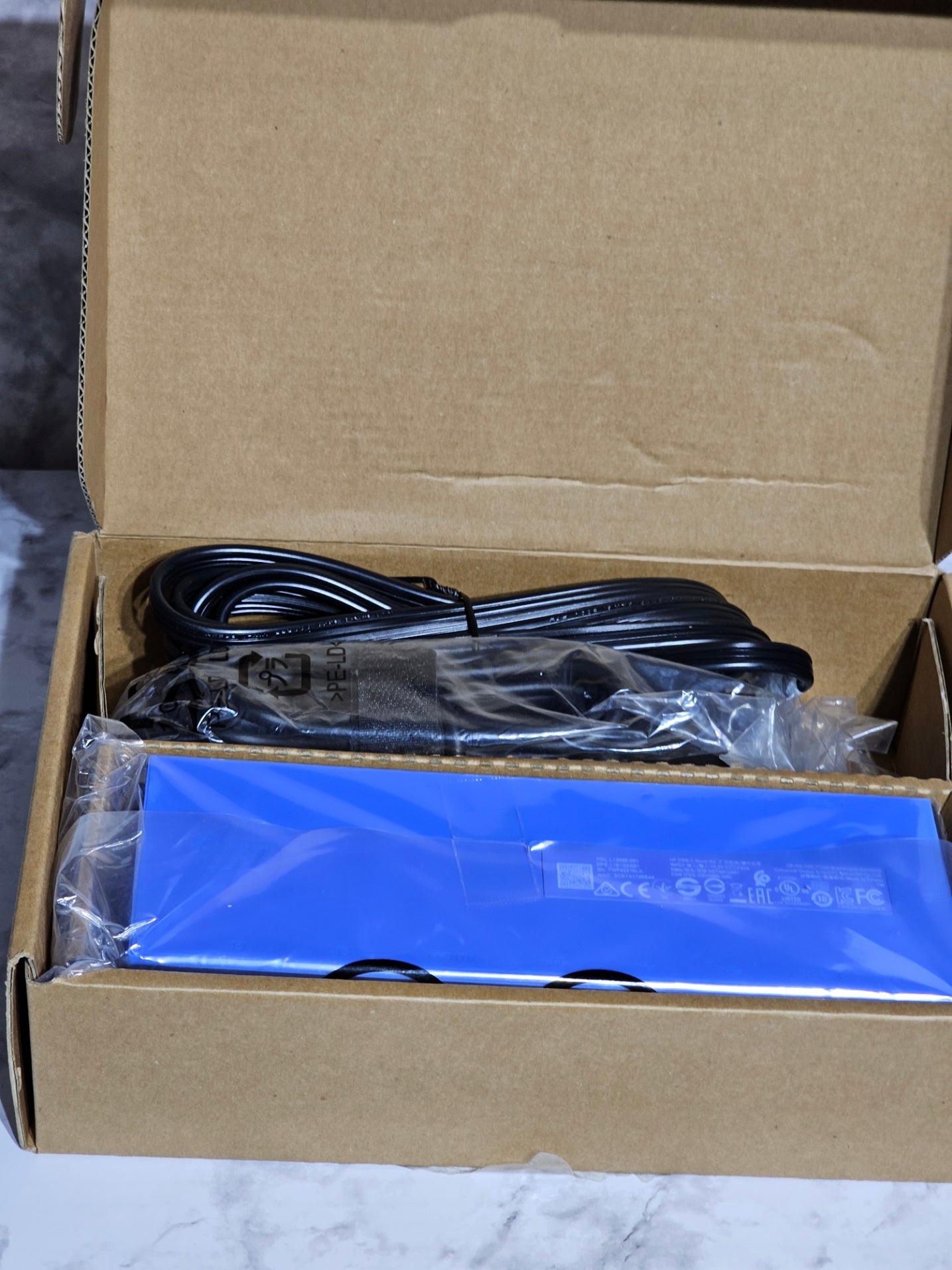 Open cardboard box with a blue electronic device and black cable inside.