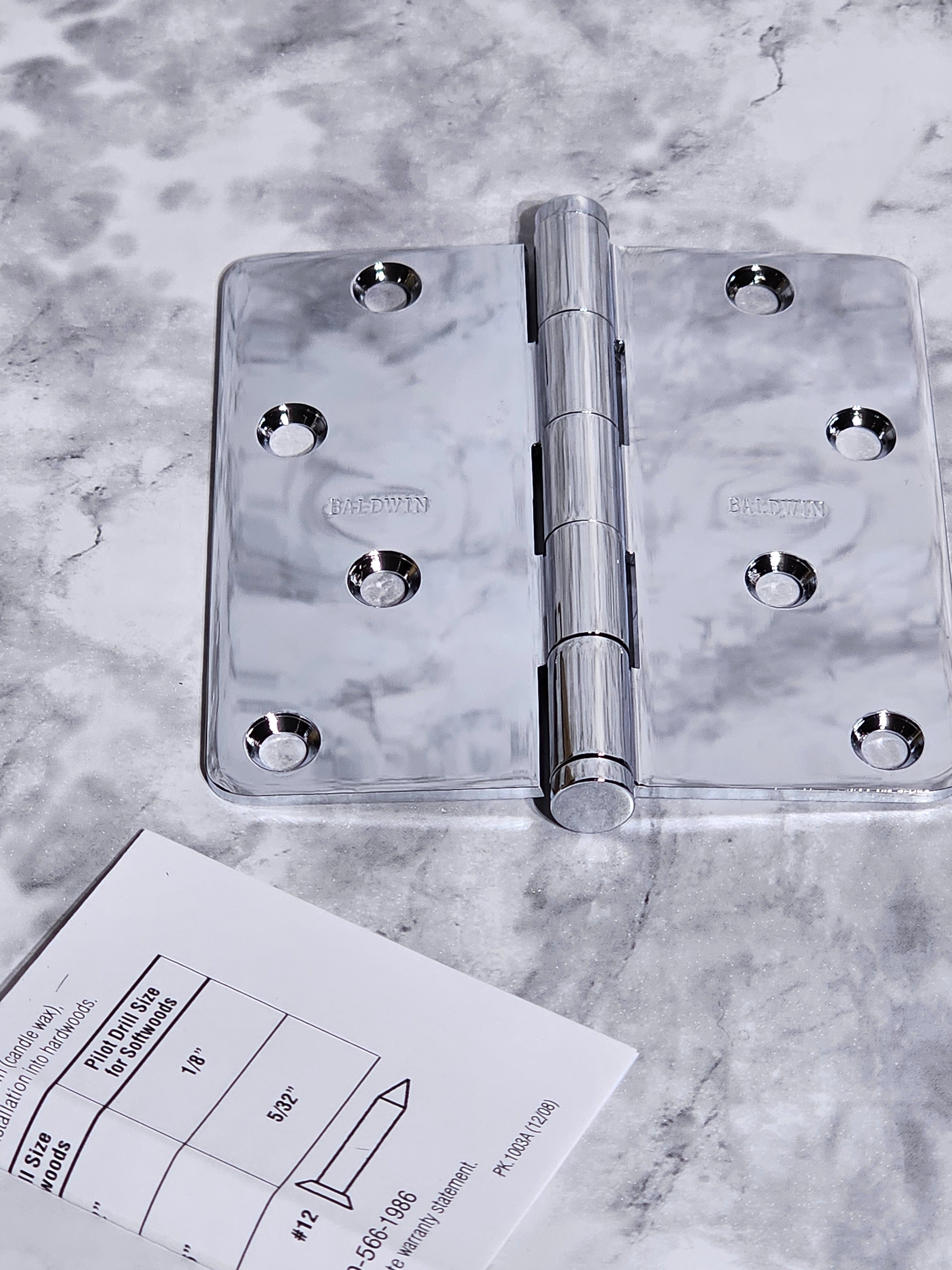 Metallic hinge on a marble surface with a technical drawing.