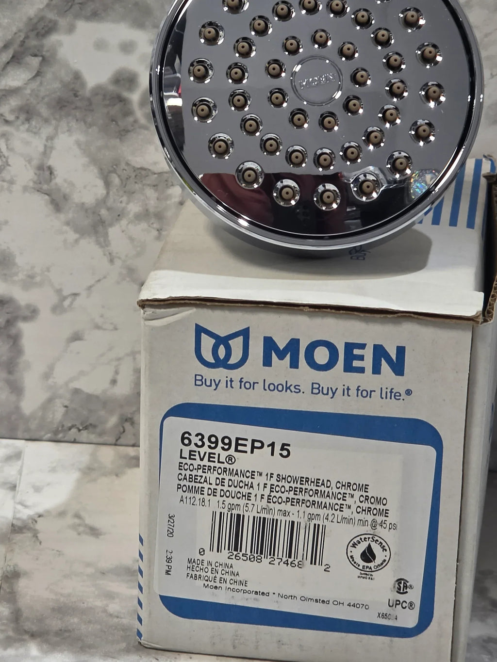 Chrome shower head with Moen packaging on a marble surface