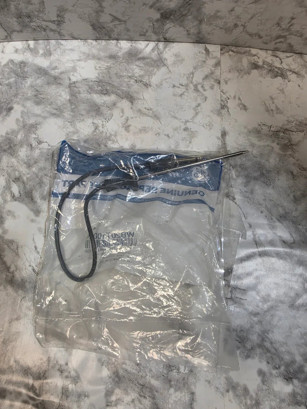 Small tool or device with a black cord in a clear plastic bag on a marble surface
