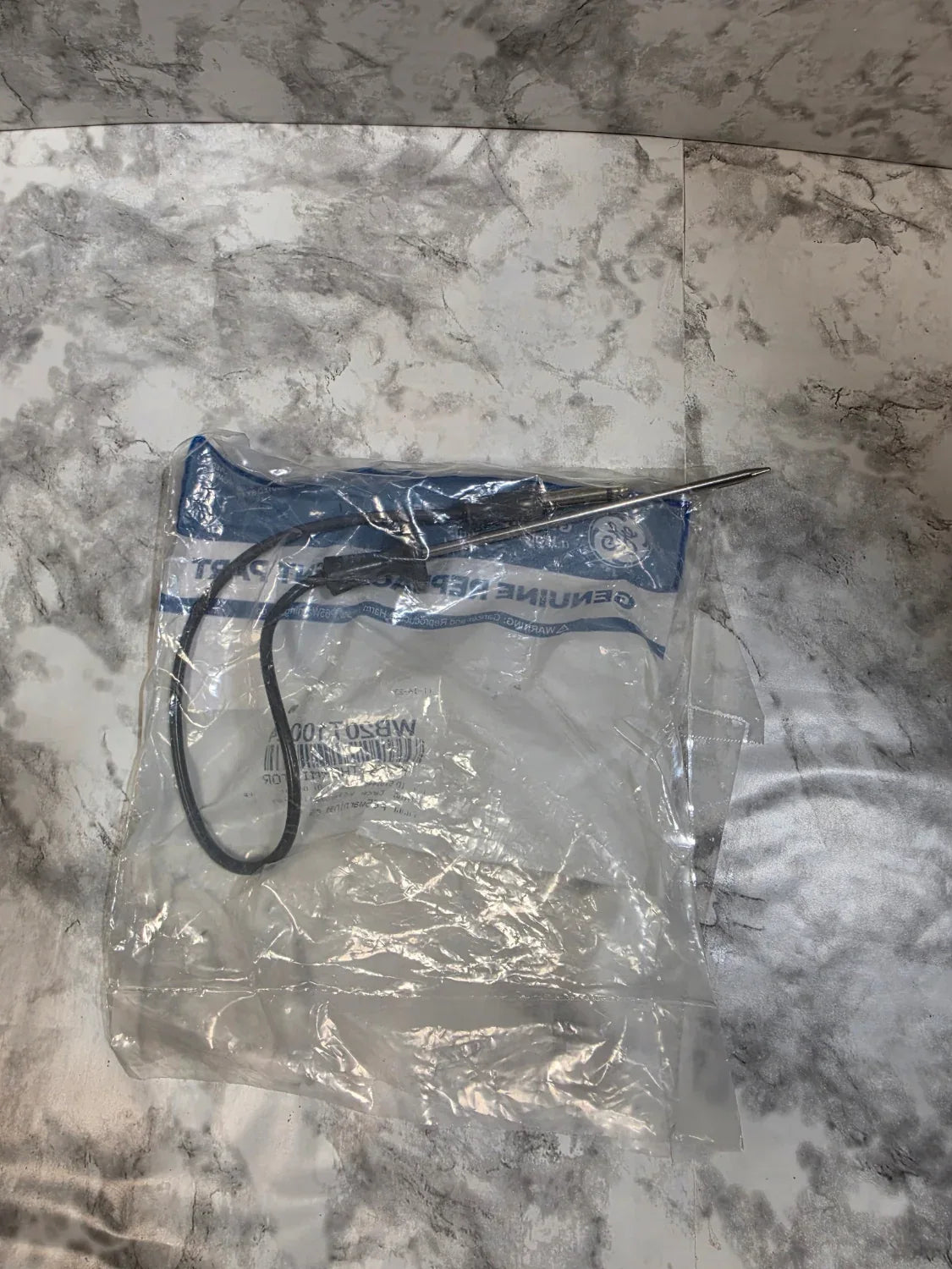 Small tool or device with a black cord in a clear plastic bag on a marble surface