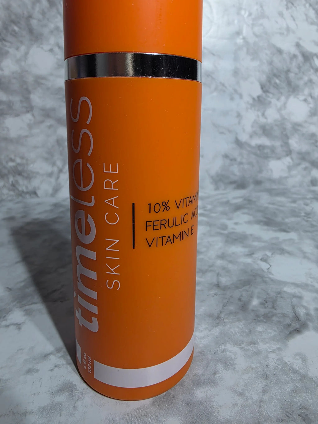 Orange skincare product tube with text on a gray marble background