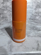 Orange skincare product with white cap on a marble surface