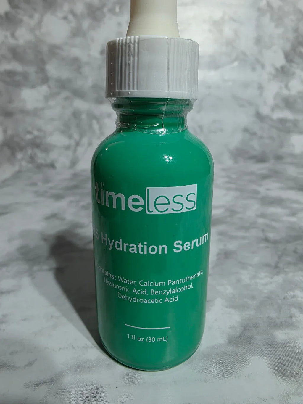 Green bottle of 'Timeless' hydration serum on a gray textured background