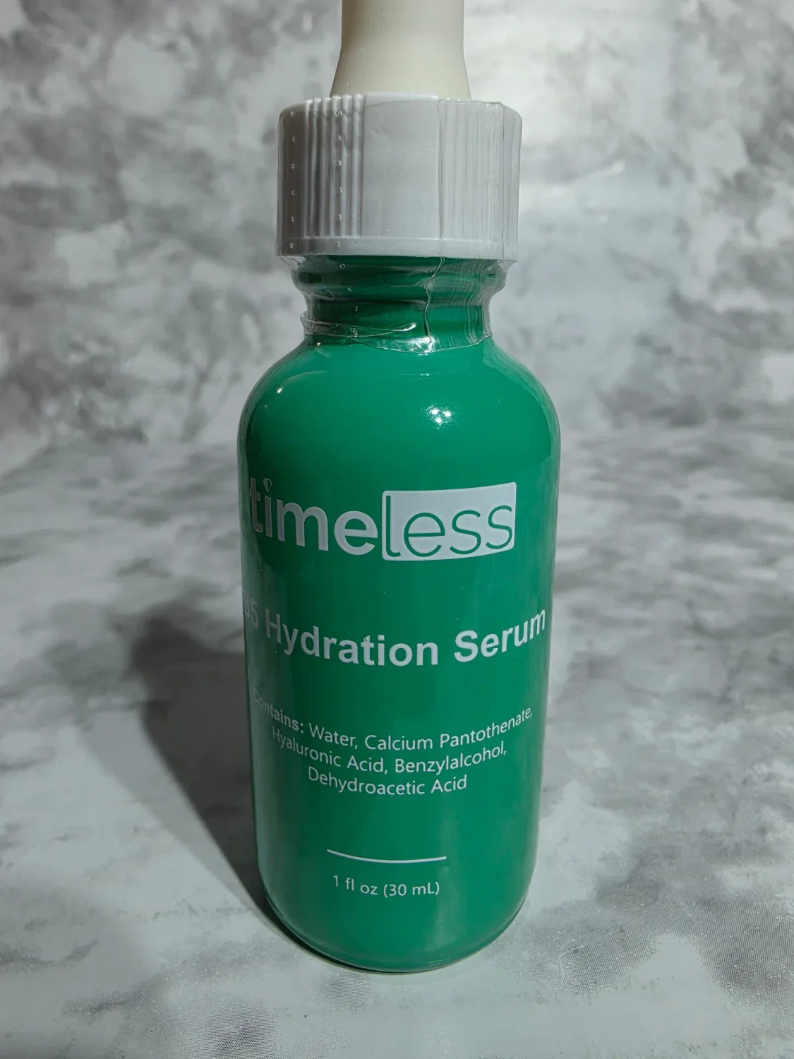 Green bottle of 'Timeless' hydration serum on a gray textured background