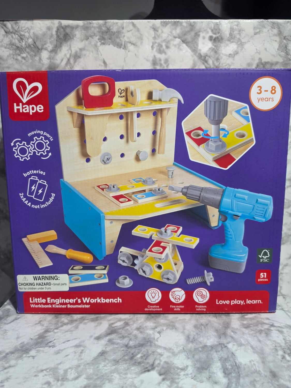 Box of a toy workbench set with tools and a drill on a marble surface