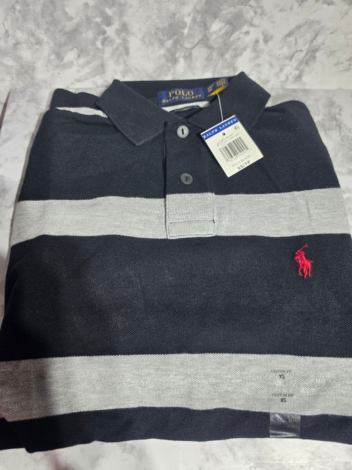 Black and gray striped polo shirt with a red logo on a textured surface