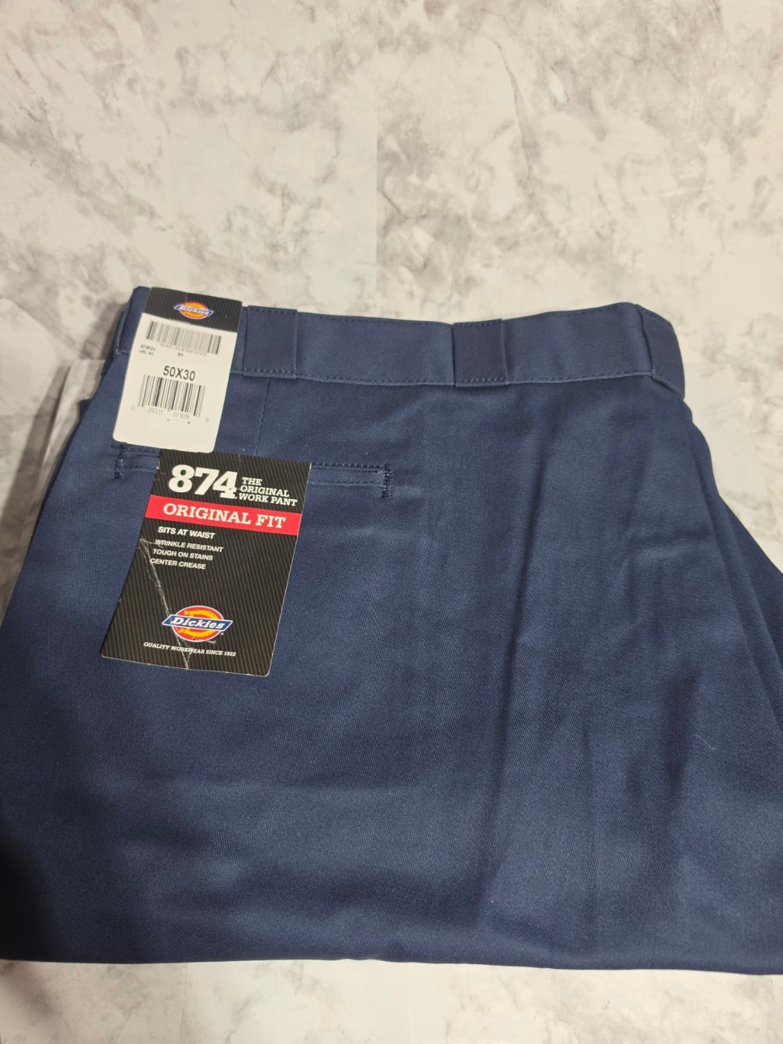 Folded navy blue pants with a 874A Original Fit label on a light gray surface
