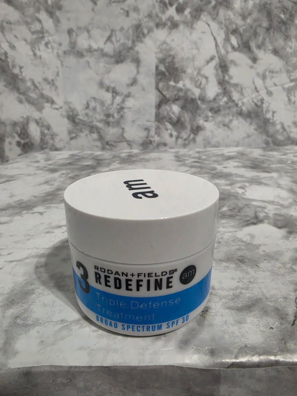 Jar of '3 Redefine' sunscreen on a textured surface