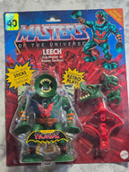 Toy figure in packaging with 'Masters of the Universe' branding on a marbled surface.