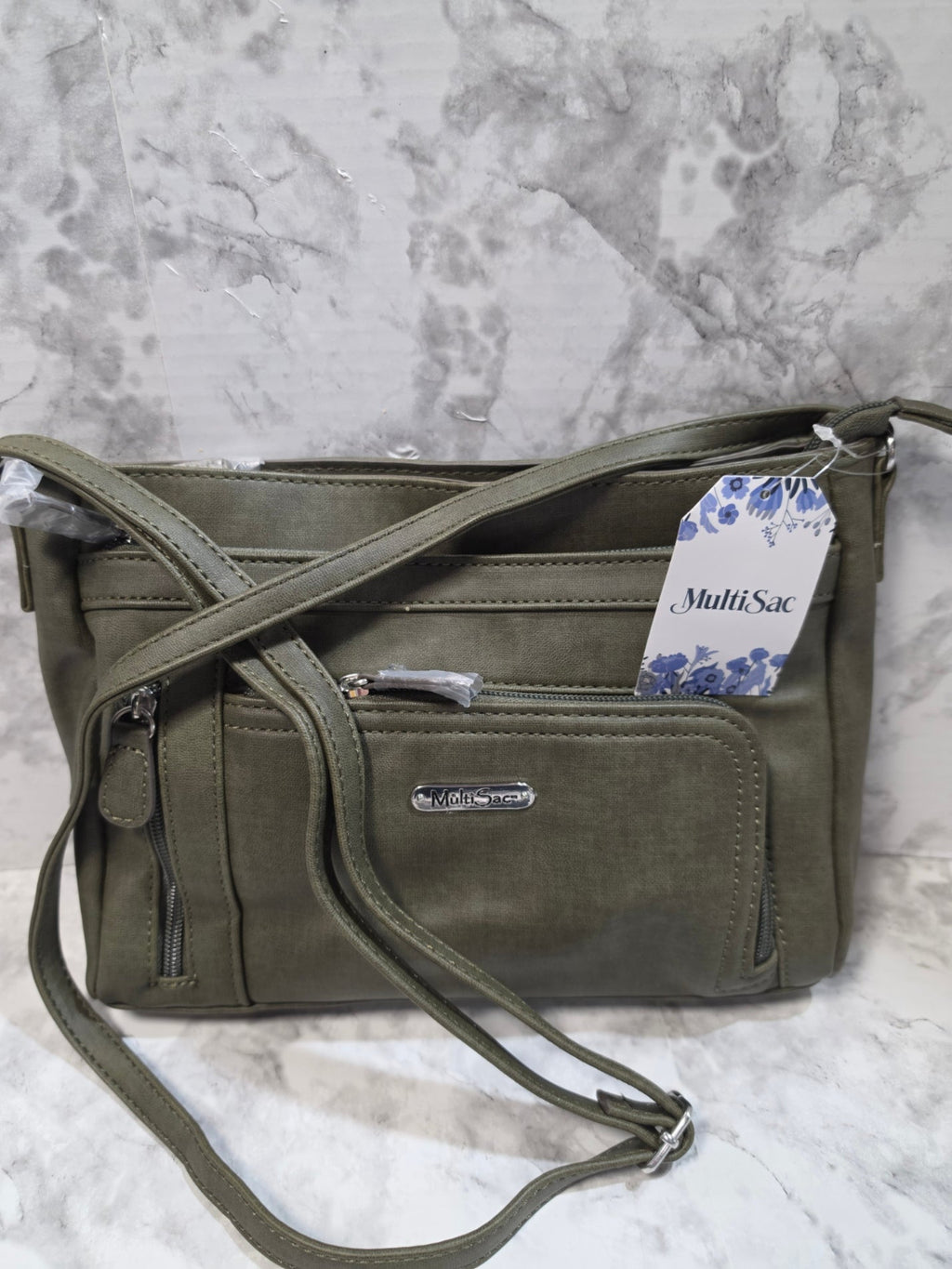 Green crossbody bag with a visible brand tag on a marble surface