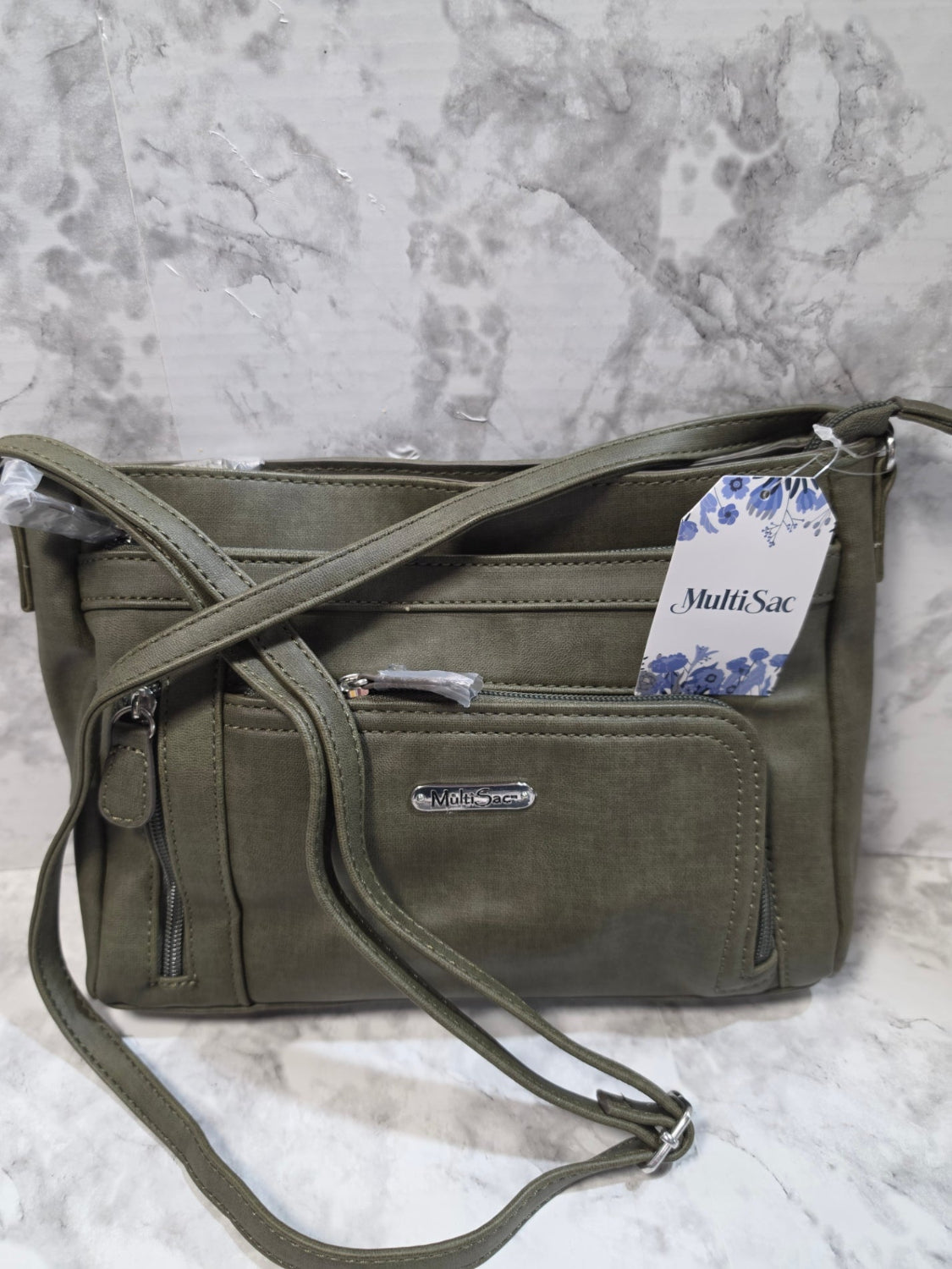 Green crossbody bag with a visible brand tag on a marble surface