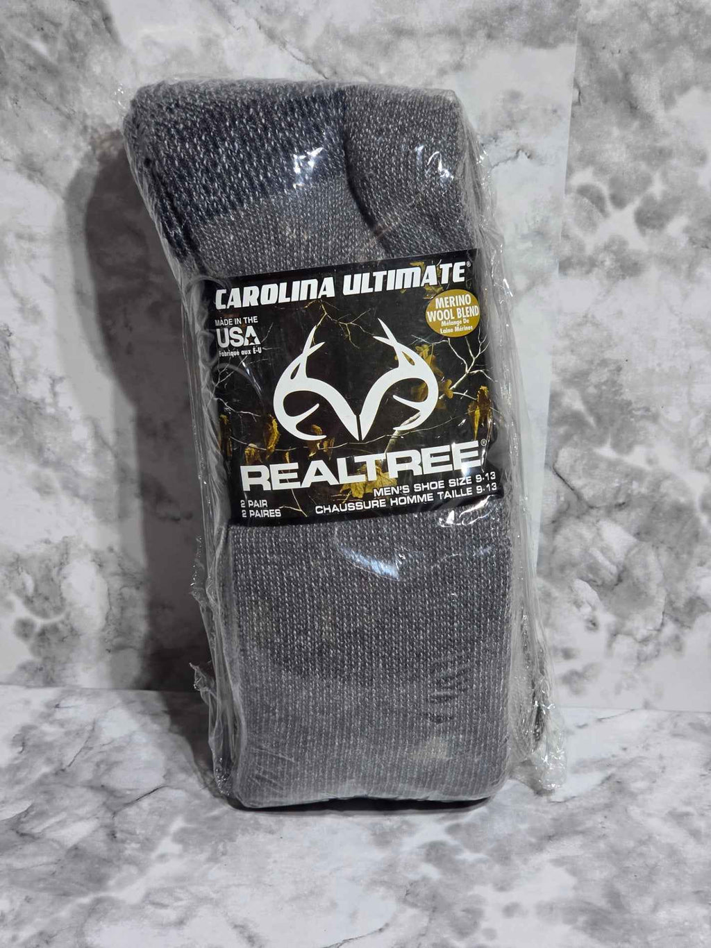 Gray socks with a Realtree logo on packaging against a gray marble background