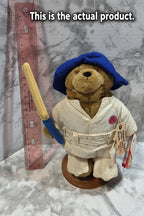 Teddy bear in a uniform with a hat and a tool, on a marble surface with a ruler for scale.