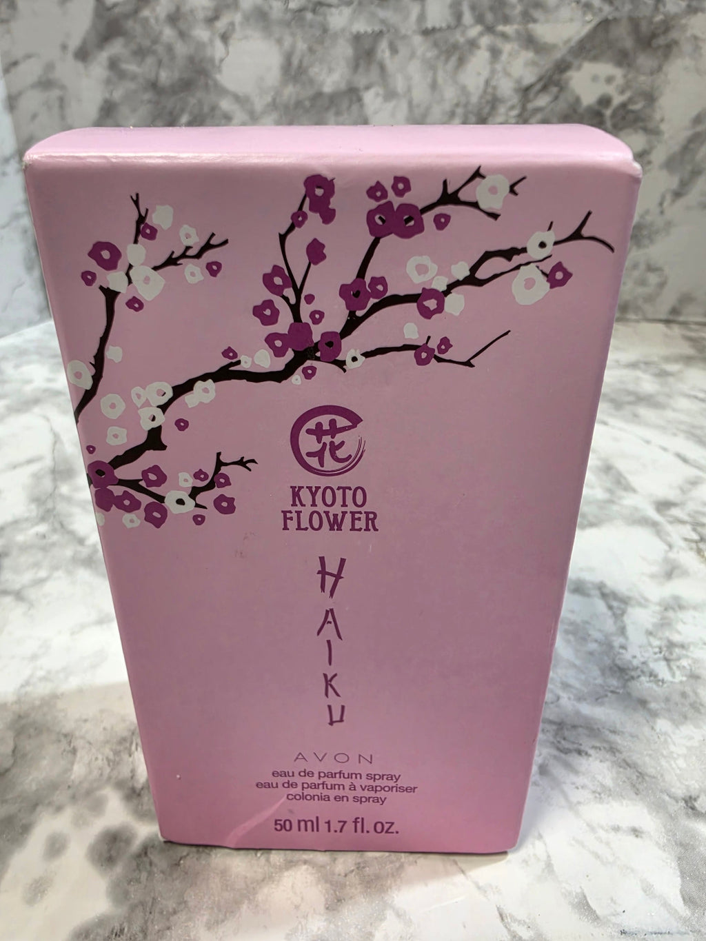 Pink product packaging with floral design and 'Avon' branding on a marble surface