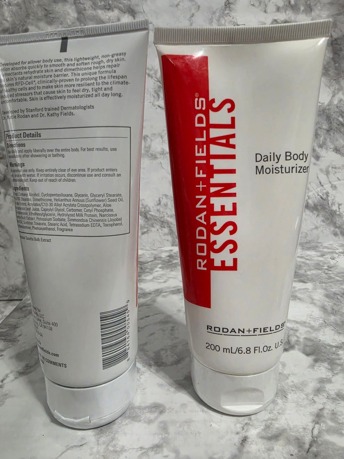 Two tubes of Rodan + Fields Essentials Daily Body Moisturizer on a marble surface.