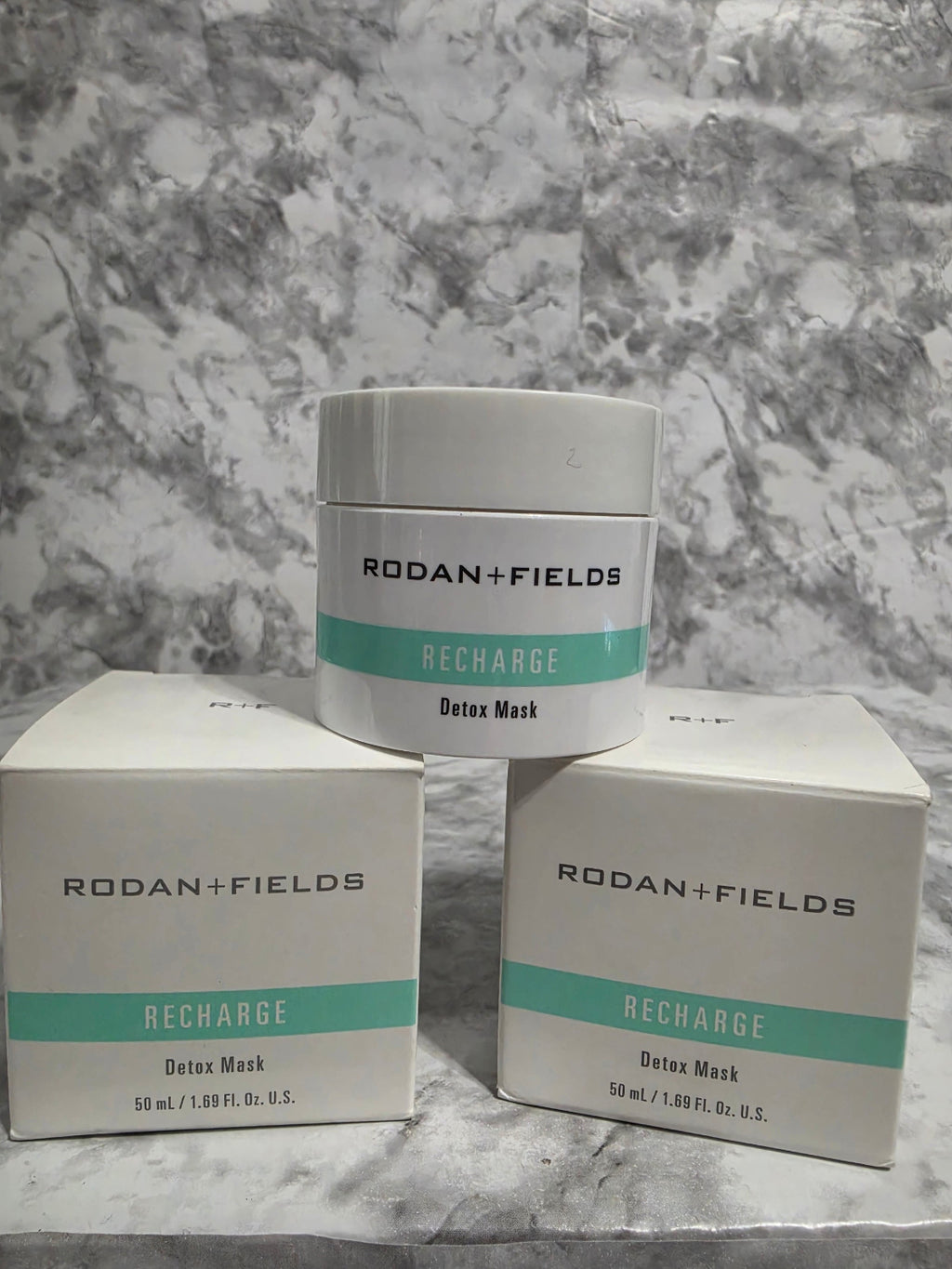 Two containers and their packaging of Rodan + Fields Recharge Deep Mask on a marble surface.