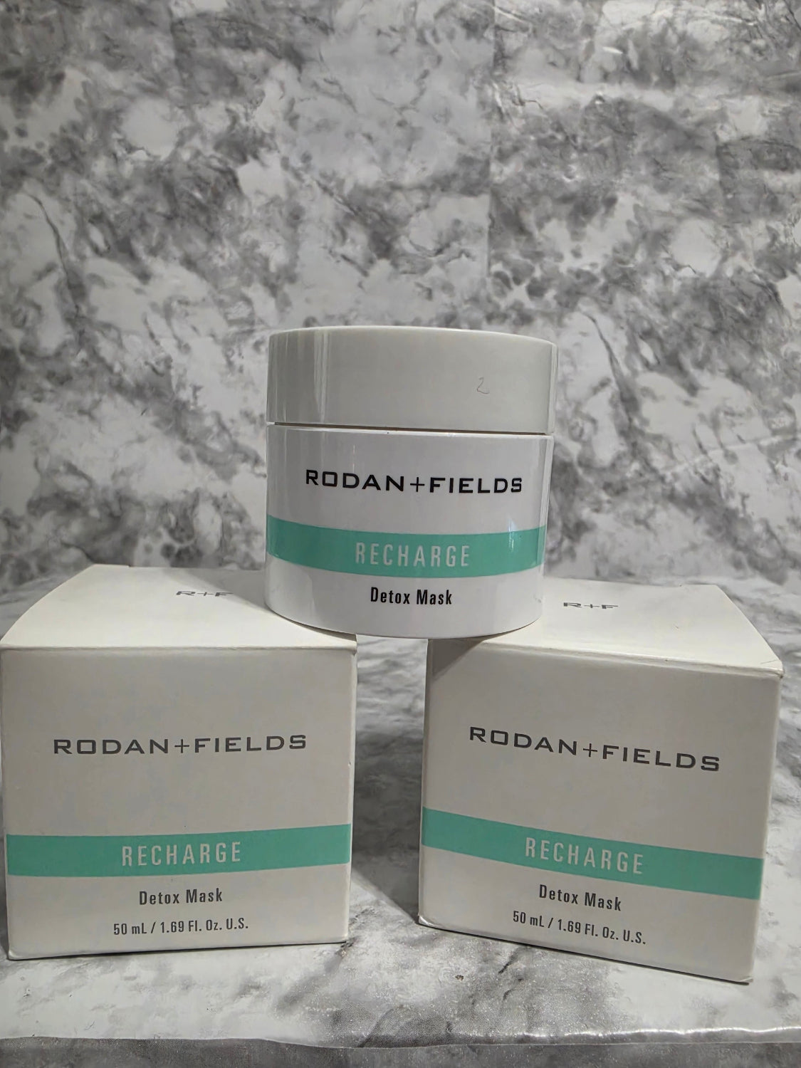 Two containers and their packaging of Rodan + Fields Recharge Deep Mask on a marble surface.