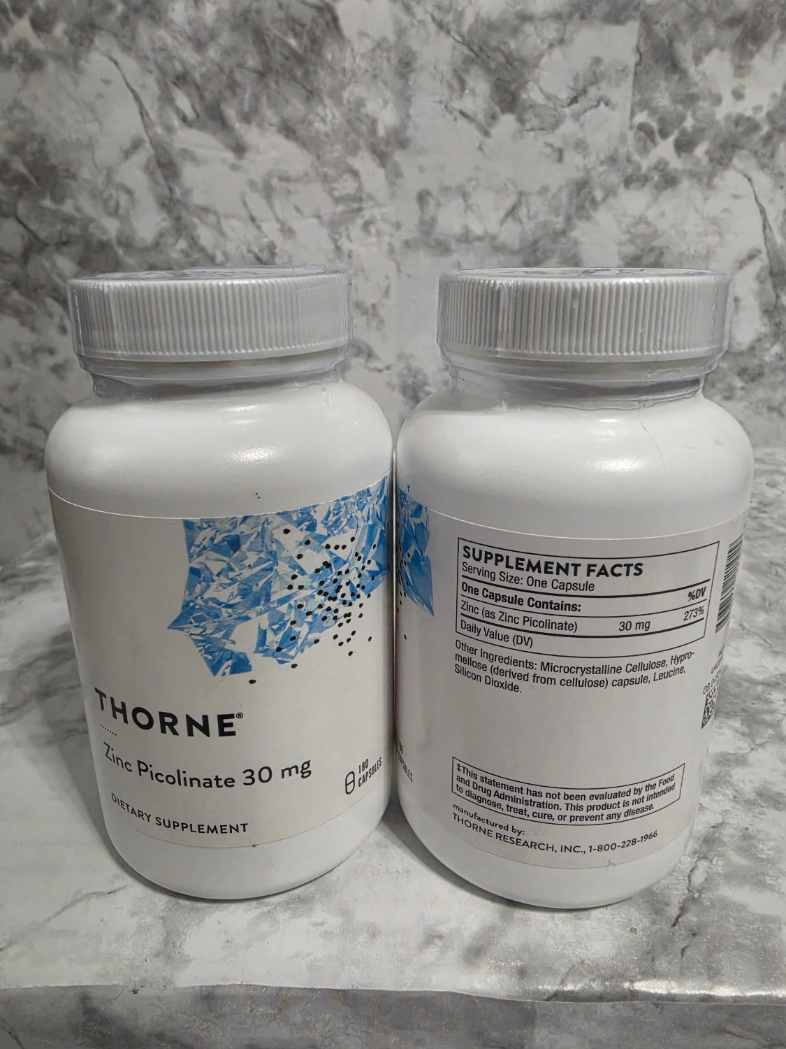 Two bottles of Thorne Research supplements on a marble surface