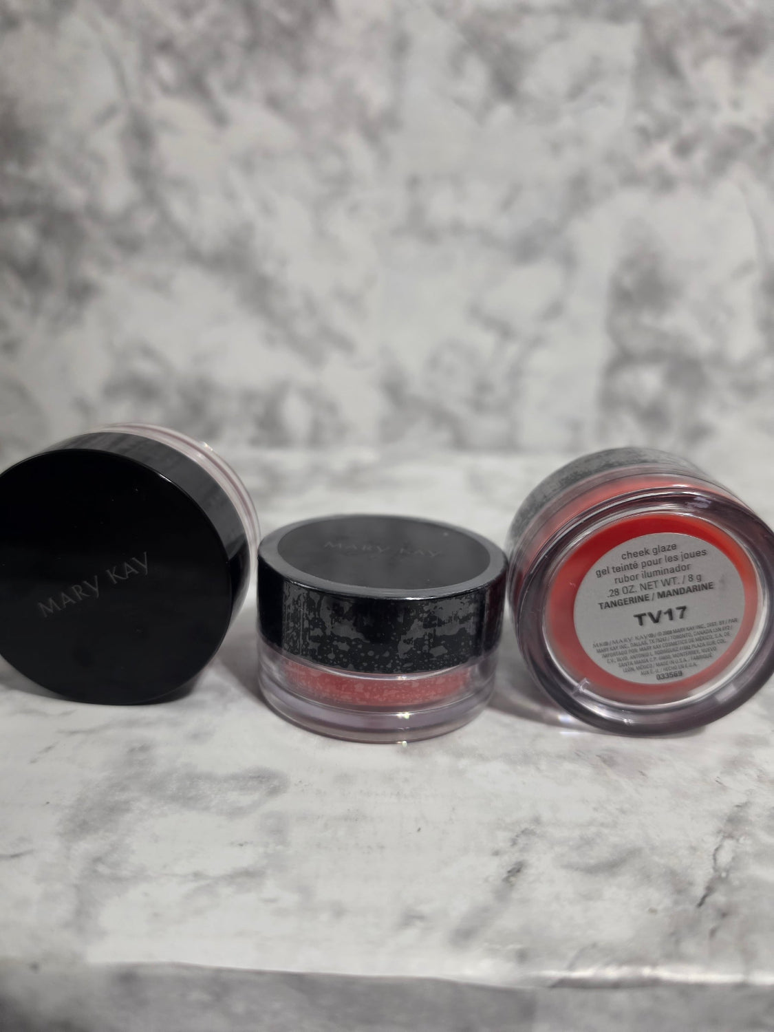 Two makeup containers with visible brand names on a marble surface