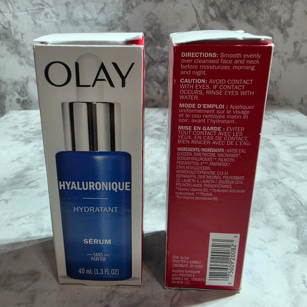 Olay Hyaluronic Serum shown with its white and blue retail box, alongside the red outer shipping carton, placed on a light gray marble-patterned surface.