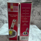 Two red and white boxes of a Prima Cucina Battery Operated Pepper Mill, stacked on a gray marble-patterned surface.