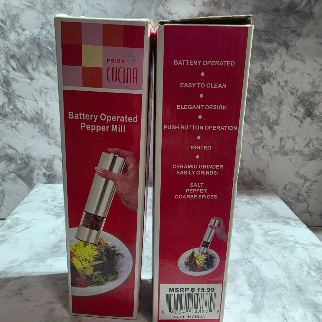 Two red and white boxes of a Prima Cucina Battery Operated Pepper Mill, stacked on a gray marble-patterned surface.