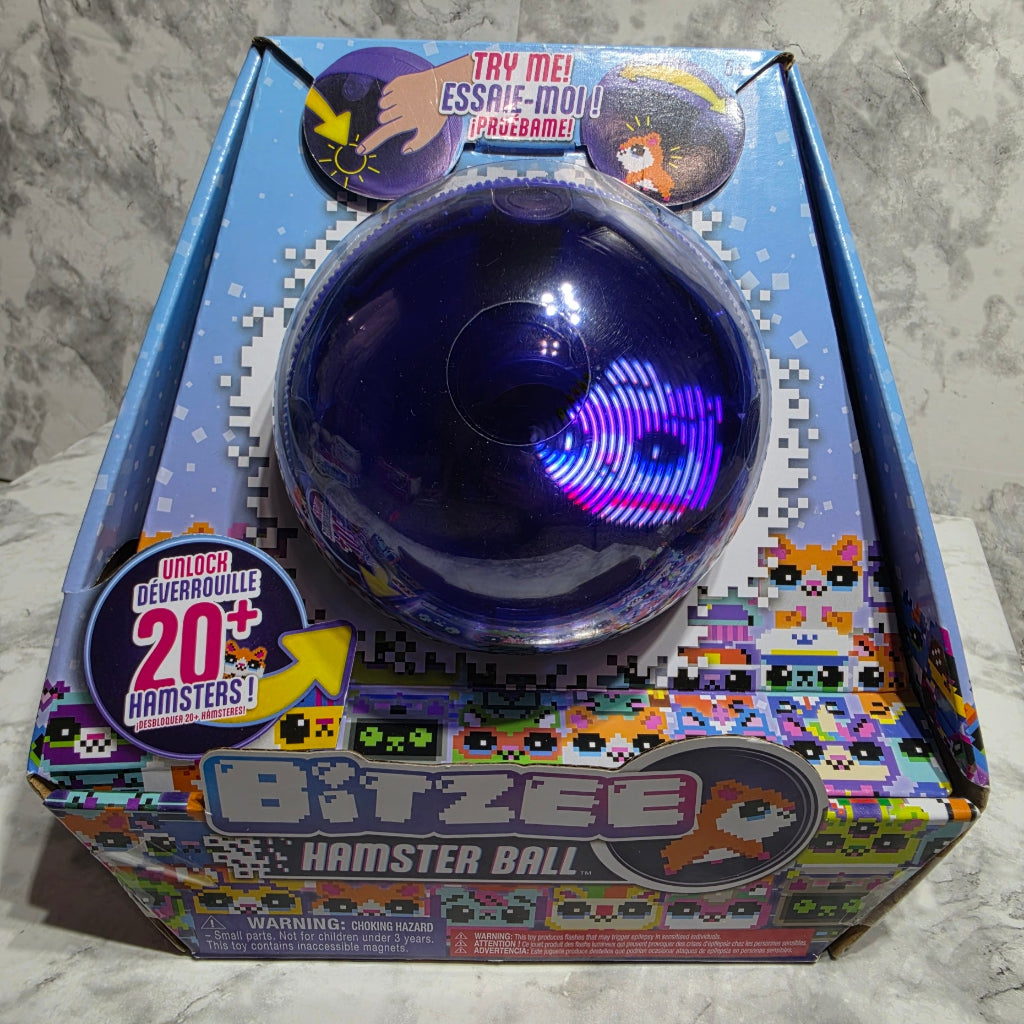 A boxed toy called Bitzee Monster Ball shown on a light stone-like surface. The package is blue and multicolored with pixel-art graphics and a large photo of the dark blue ball on the front.