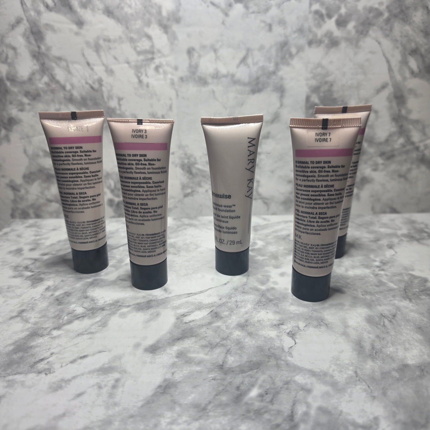 Mary Kay TimeWise Luminous-Wear Liquid Foundation tubes showing multiple shades including Ivory 3, Ivory 7, and Bronze variants on marble surface