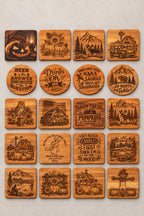A display of various Halloween-themed engraved wooden coasters, signs, and wall art arranged on a table, with a person's legs visible at the bottom edge.