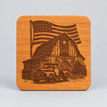 A square wooden coaster held in hands, featuring a laser-engraved design of a vintage pickup truck, a barn with an American flag, and a star on the barn door.