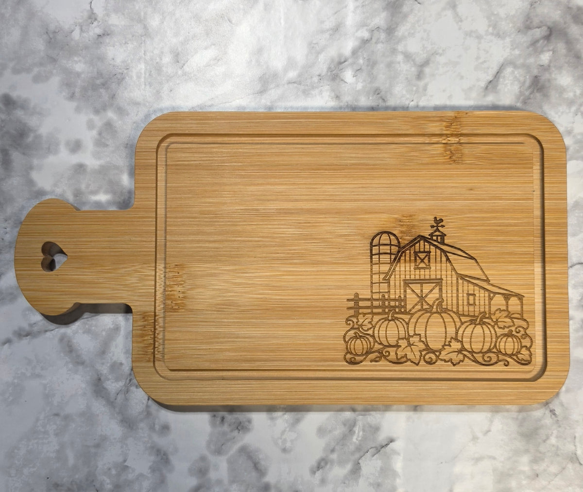 Actual engraved bamboo heart-handle board with a farmhouse barn and pumpkins.