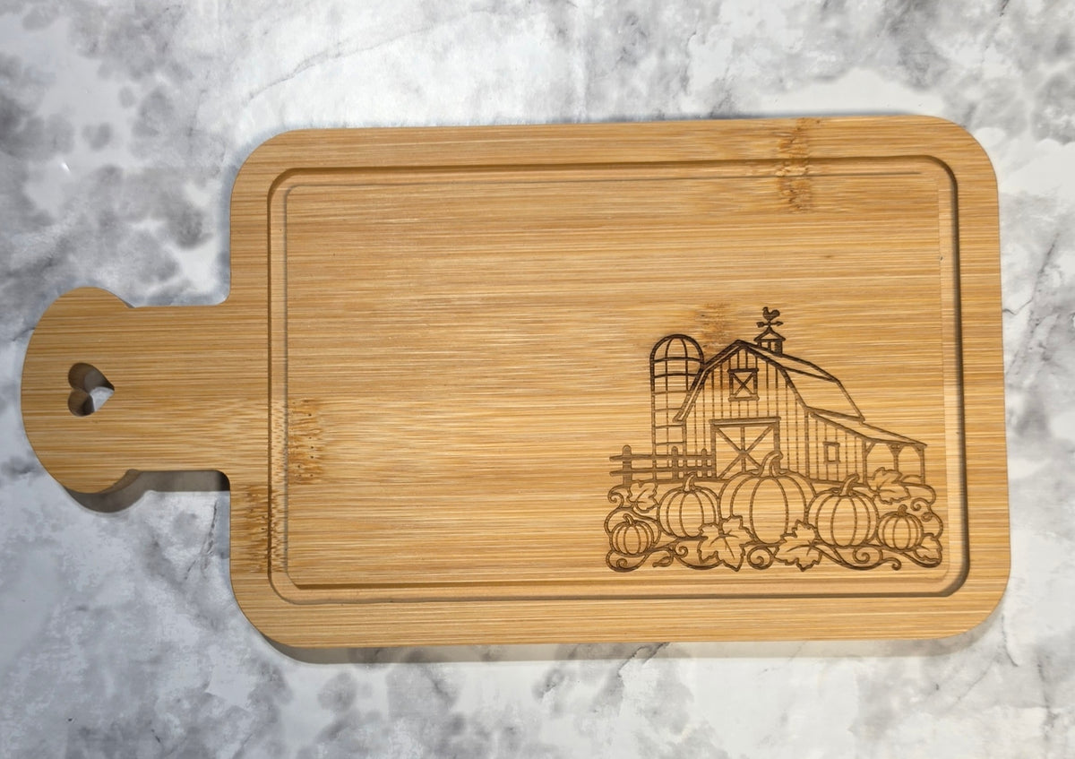 Actual engraved bamboo heart-handle board showing the farmhouse barn and pumpkin design.