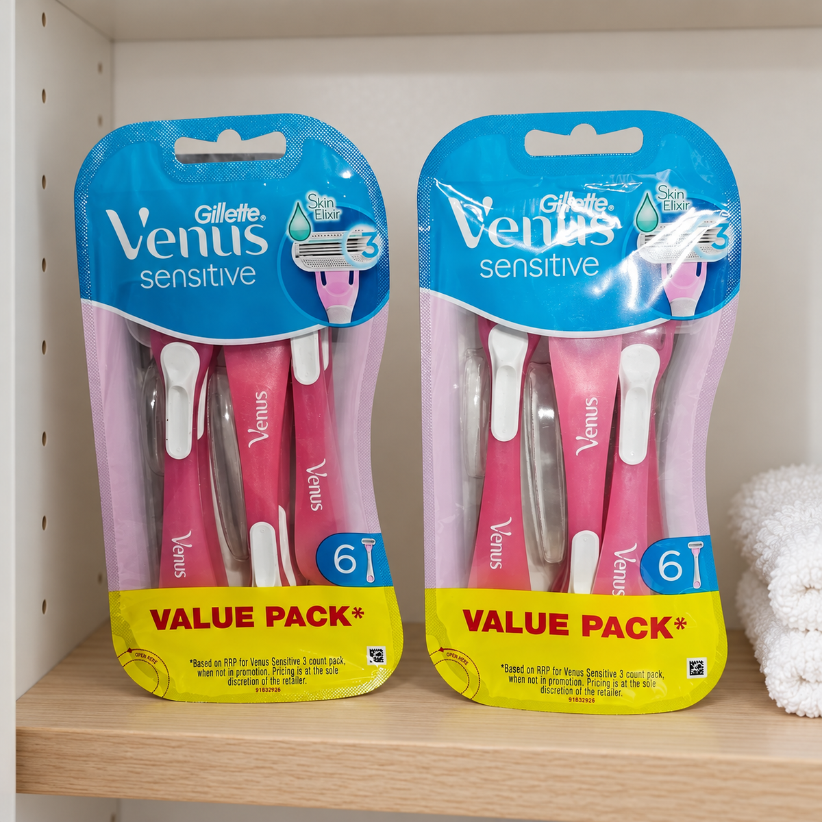 Two Gillette Venus Sensitive six-count value packs on a bathroom cabinet shelf beside a white towel