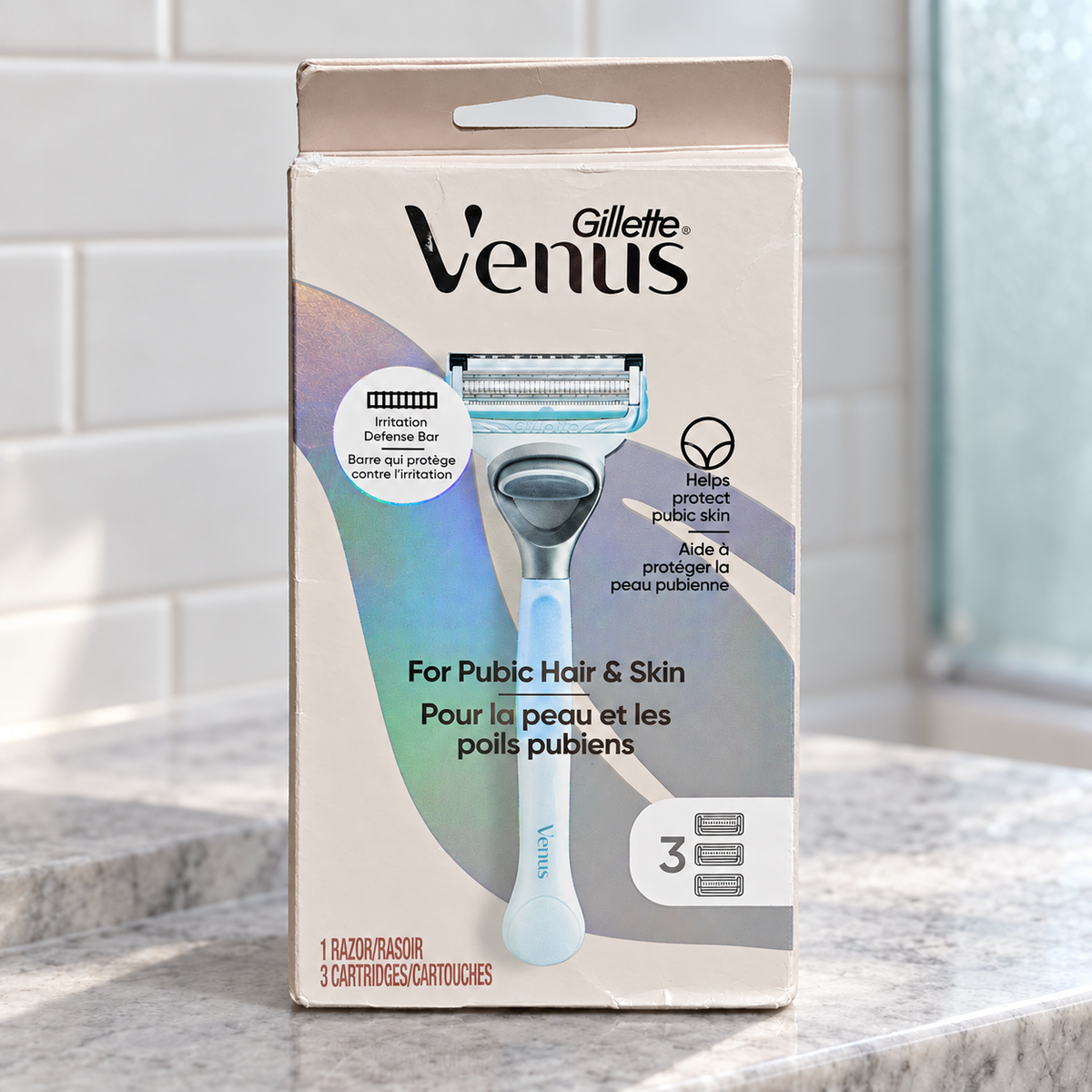 Gillette Venus Pubic Hair & Skin kit with one handle and three cartridges on a gray bathroom ledge against a tiled wall