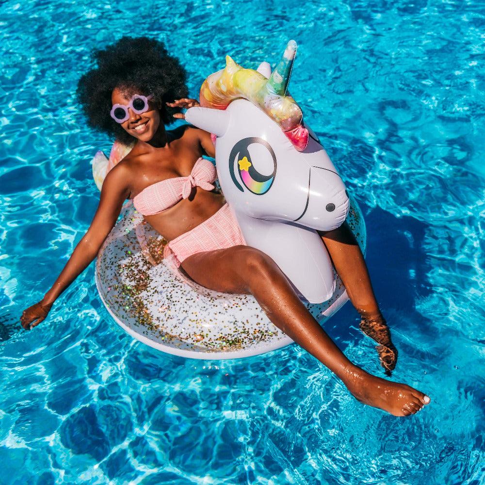 Adult relaxing in a PoolCandy Glitter Unicorn pool tube in a swimming pool