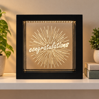 Black Congratulations LED light box displayed on a shelf beside books and plants