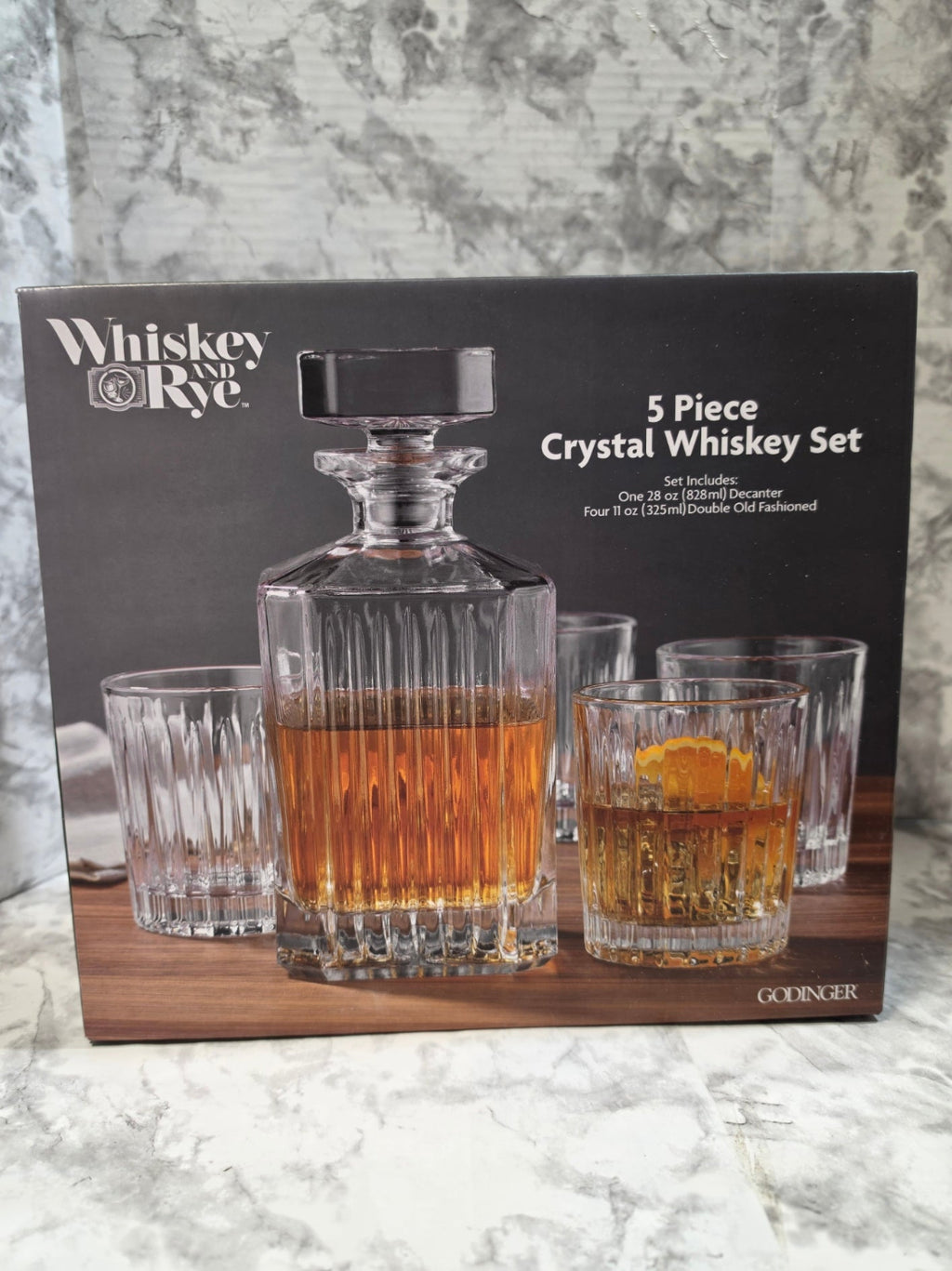 5-piece crystal whiskey set with decanter and glasses on a branded box against a marble background
