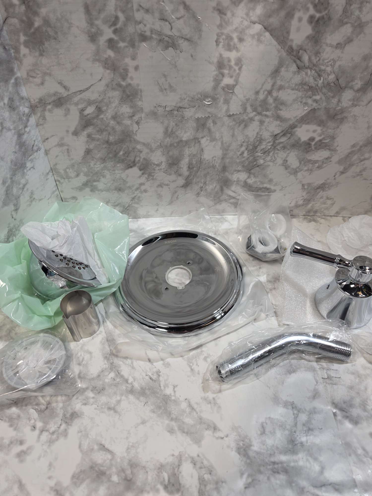 Set of bathroom fixtures including a shower head, drain cover, and faucet on a marble countertop.