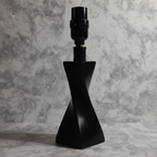 Architectural silhouette of matte black twisted lamp base reflecting soft evening light against neutral background